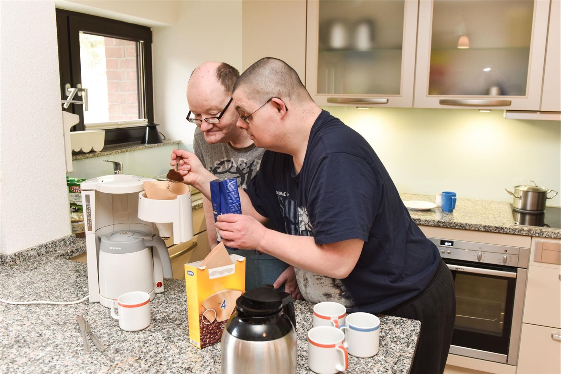 Zwei Männer mit Behinderung bereiten gemeinsam Kaffee zu