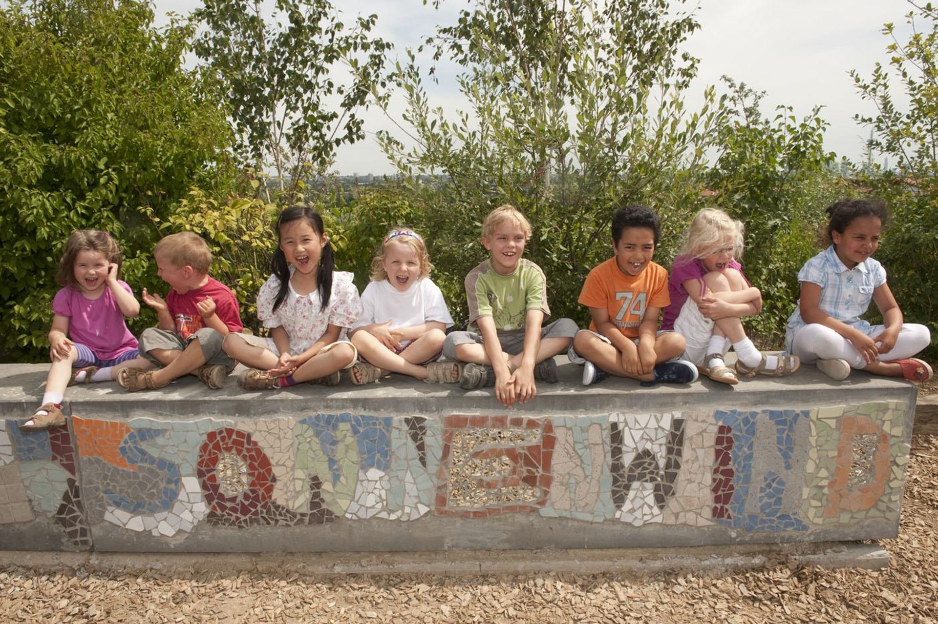 Eine Reihe Kinder steht hinter einer bunt bemalten Mauer