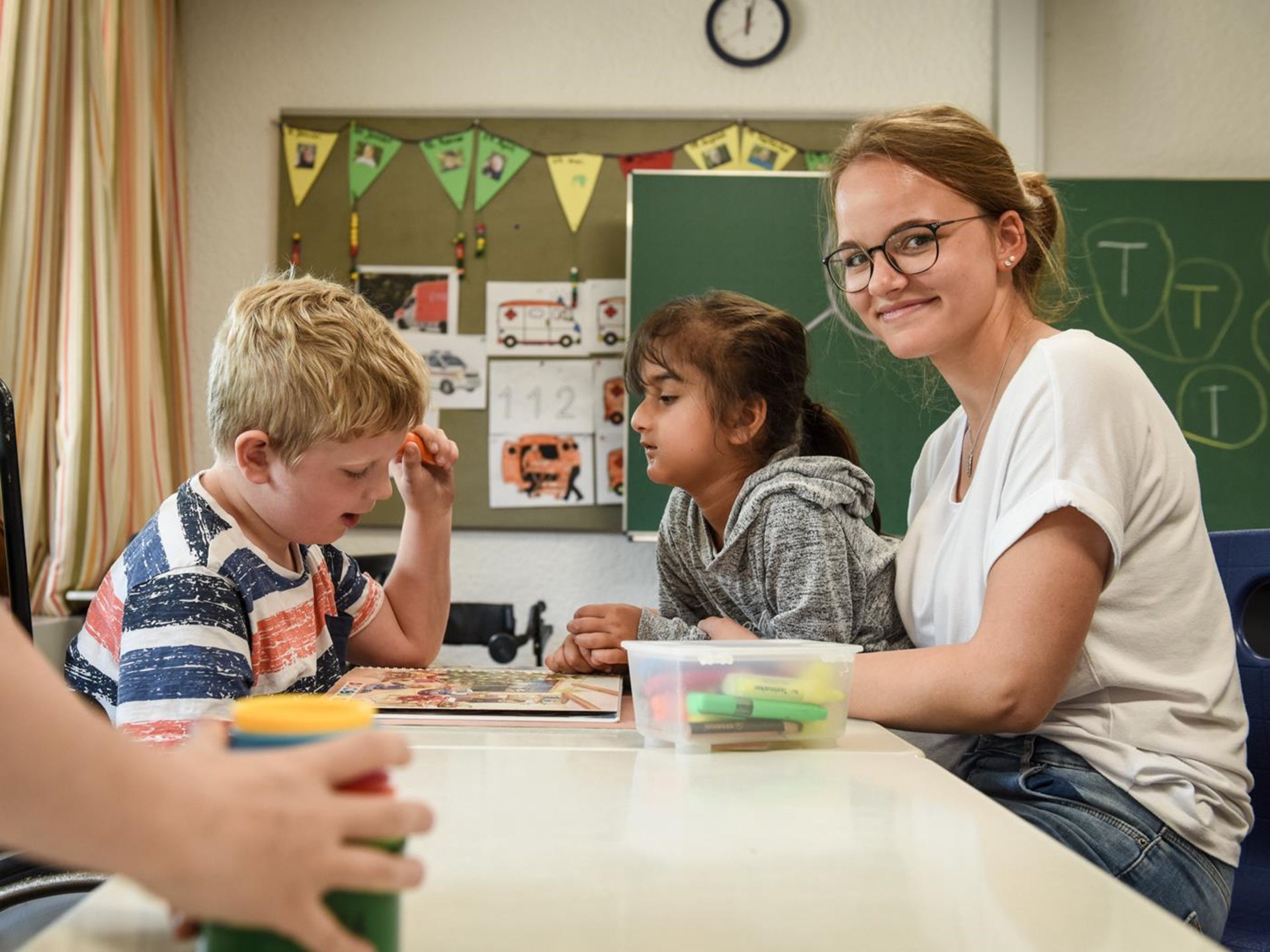 Eine Freiwillige sitzt gut gelaunt mit drei Kindern mit geistiger Behinderung am Tisch